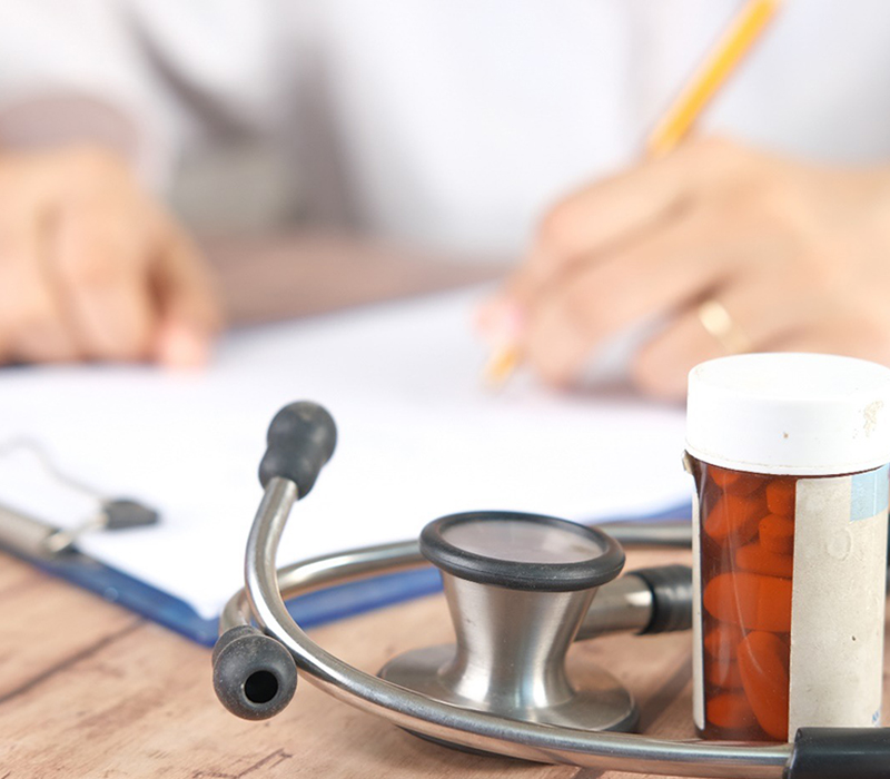 Hands writing on paper next to a stethoscope and medication bottle