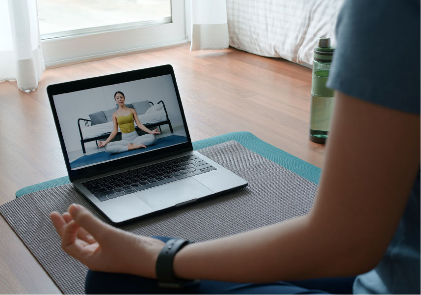 Person sitting on yoga mat with laptop showing virtual mind-body class