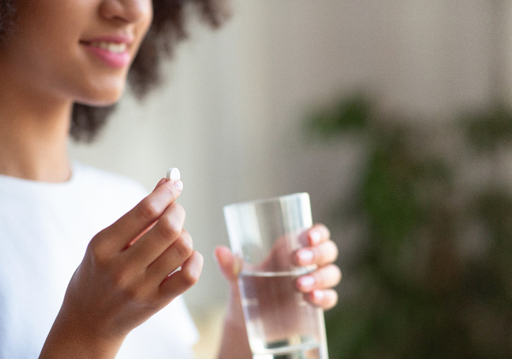Black female patient holding a pill capsule and a glass of water