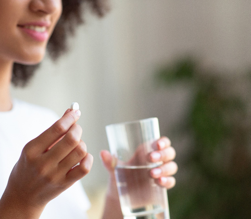 Black female patient holding a pill capsule and a glass of water