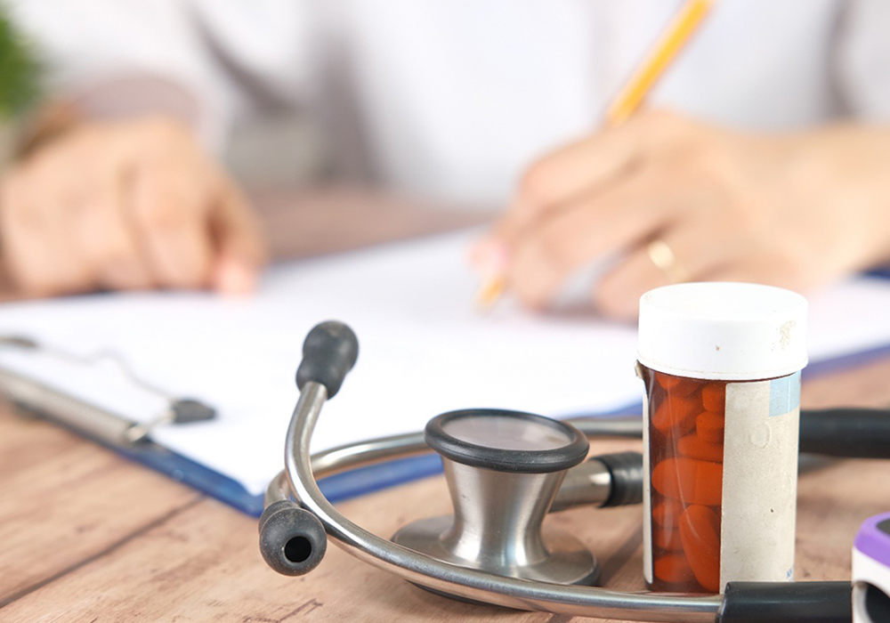 Hands writing on paper next to a stethoscope and medication bottle