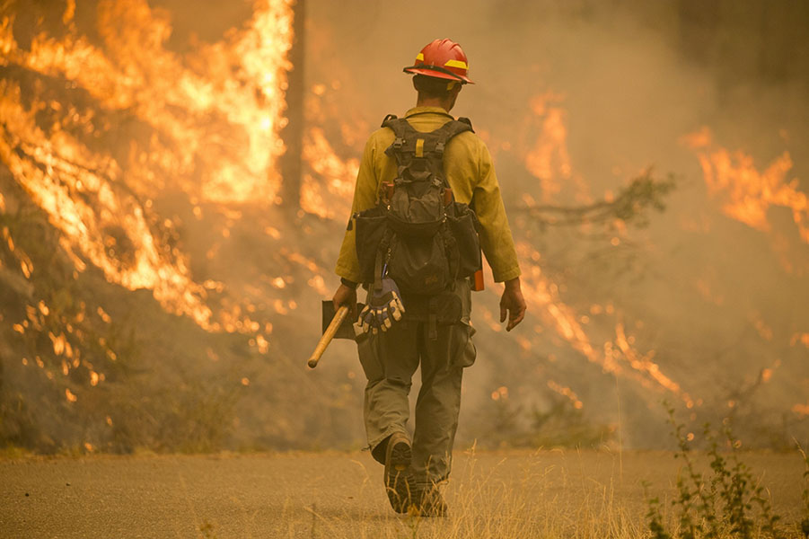lone firefighter walking away with flames in background