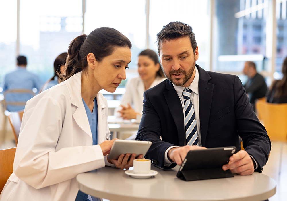 nurse sitting with man in a suit looking at computers