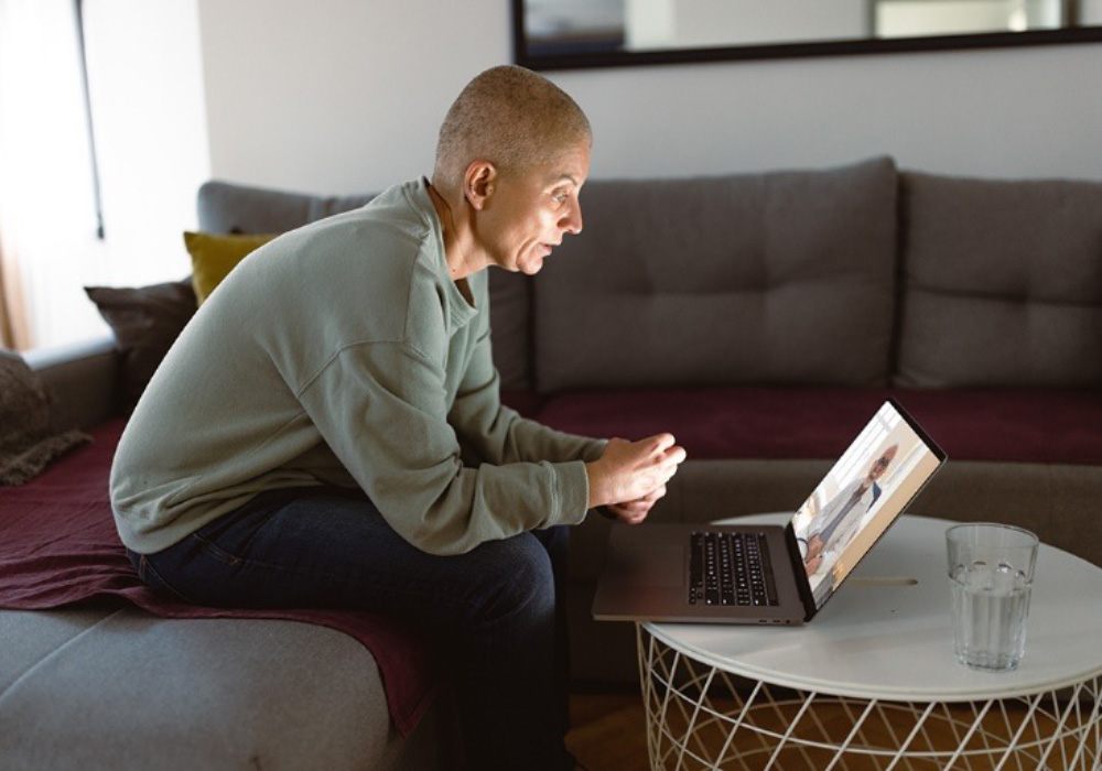 cancer patient sitting with laptop and a glass of water on round desk