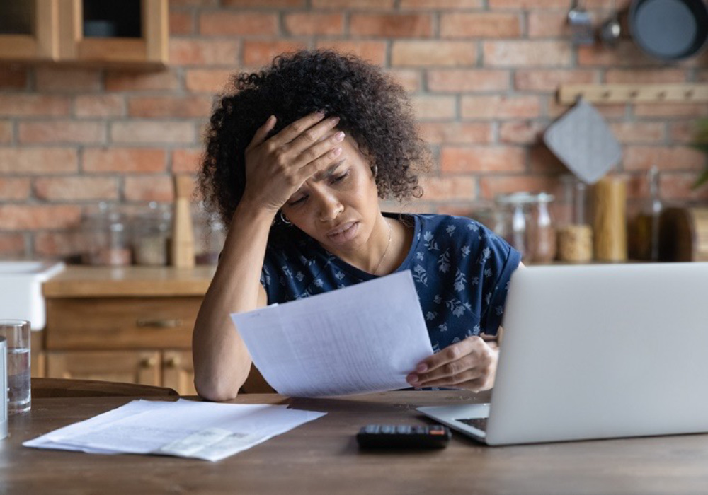 black patient looking at bill frustrated while sitting on desk with laptop and papers in front of her