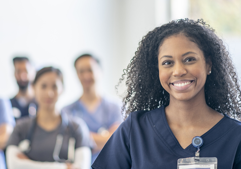 black nurse smiling with other nurses in the background blurred