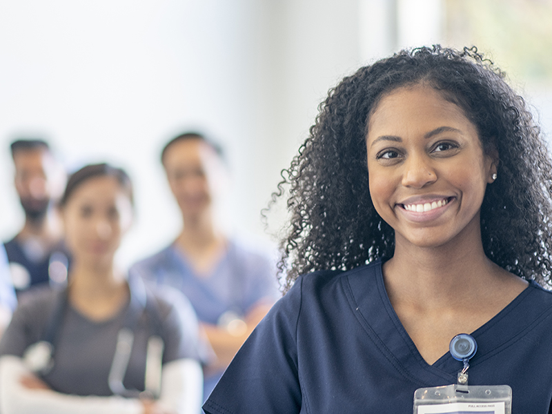 black nurse smiling with other nurses in the background blurred