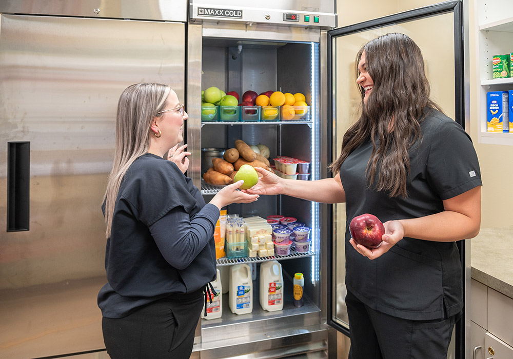 Nurse handing fruit to another nurse at a refrigerator